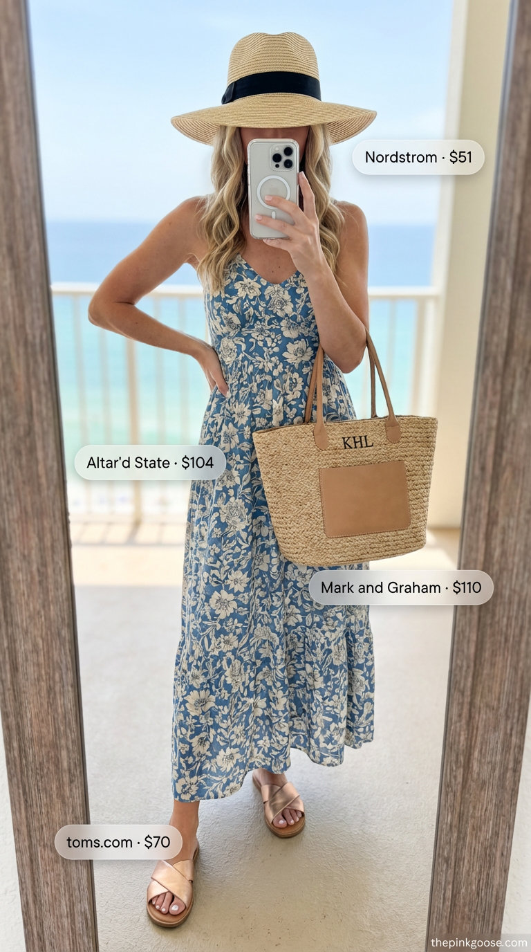 A woman poses in a soft blue and cream floral maxi dress, rose gold slide sandals, a wide-brim straw hat, and a woven straw tote bag, defining chic summer beach outfits for women 2026.