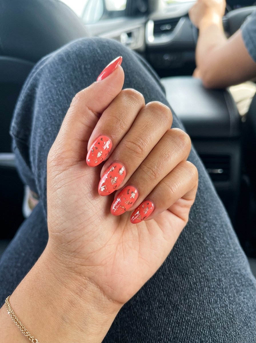 Vibrant Coral Foil Almond Nails Summer 2026 Vibrant coral almond nails with metallic foil flakes for summer 2026 vacation style.