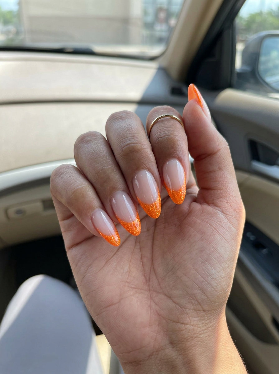 Vivid orange glitter French tips on almond nails for a glamorous date night, a festive neon summer nails 2026 choice.