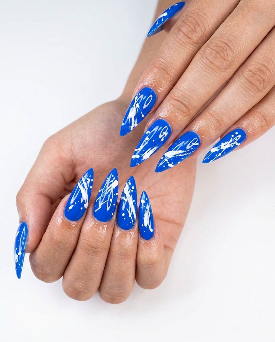 Edgy electric blue stiletto nails with abstract white paint splatters. Stiletto summer nails 2026.