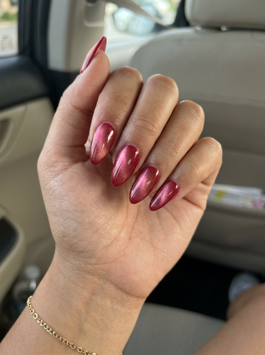 Glamorous almond nails in deep strawberry red with a shifting pink-gold magnetic cat-eye effect. Summer strawberry nail ideas 2026.