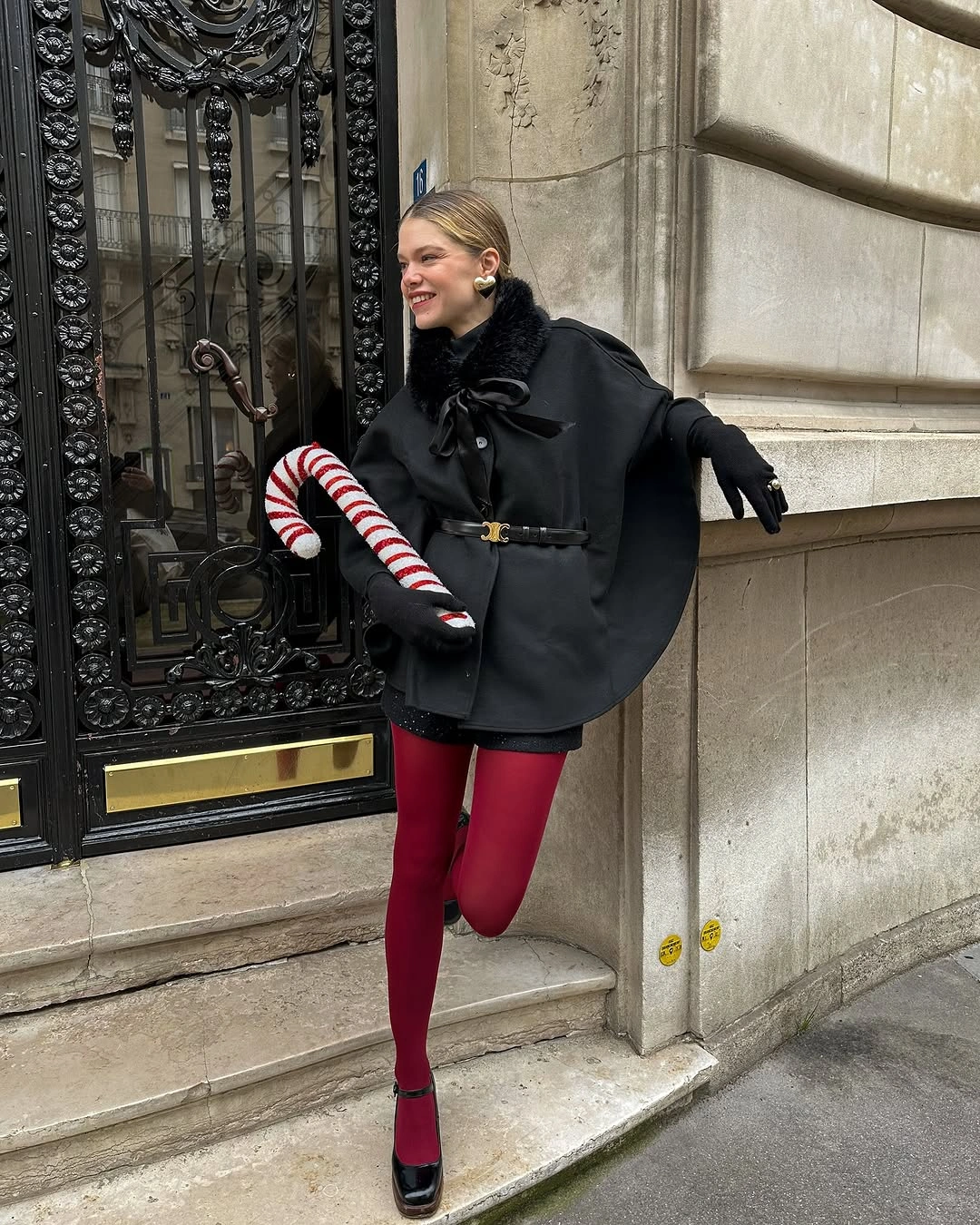 chic christmas outfits 2026 Black Cape Red Tights and a Playful Parisian Mood