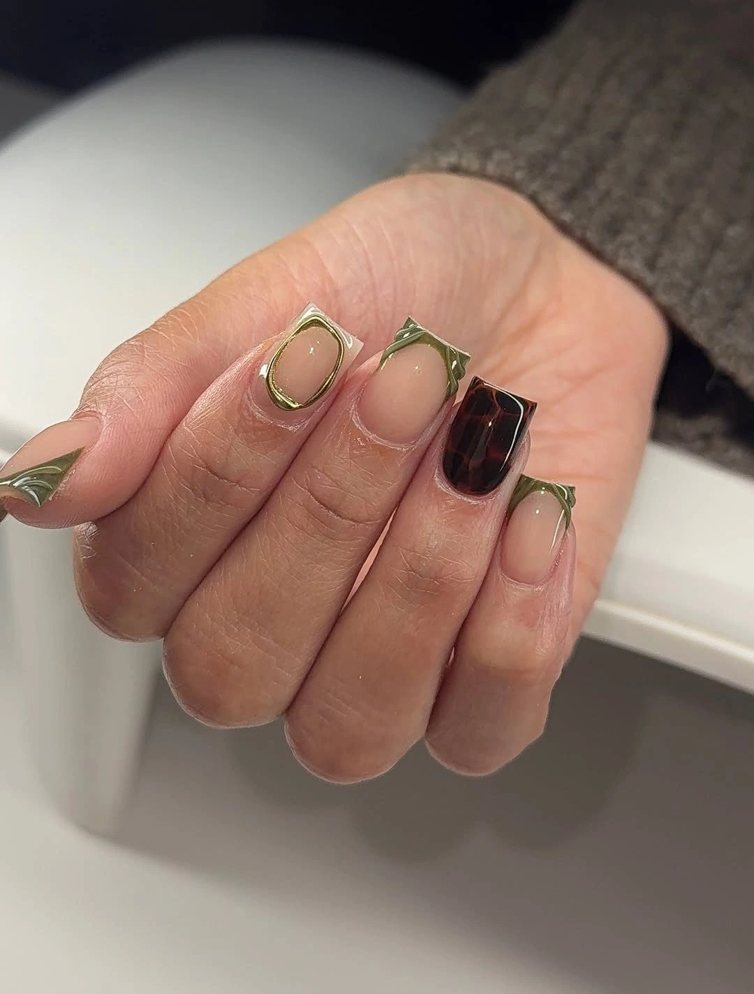 Short square nude nails with olive outlines and dark checkered accent Short square nude nails with olive outlines and dark checkered accent